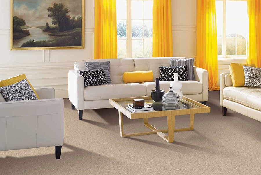 Living room with white couches on tan carpet accented by yellow curtains and throw pillows.