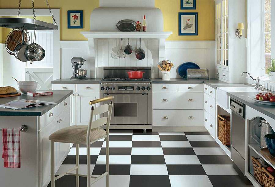 An older kitchen with a modern makeover to provide a retro look with modern stainless steel appliances on checkerboard themed luxury vinyl tile floors.