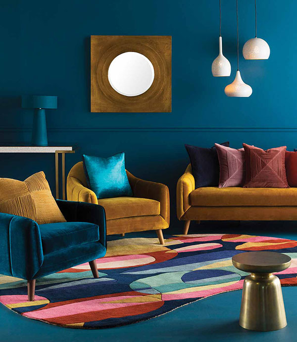 A living room filled with Memphis design themed accessories to a large colorful area rug, blue carpet, and blue and gold chairs.