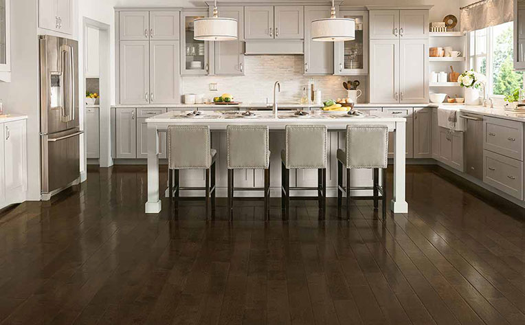 Open kitchen design with dark stained wood floors, an island with bar-style seating and trendy overhead lights 